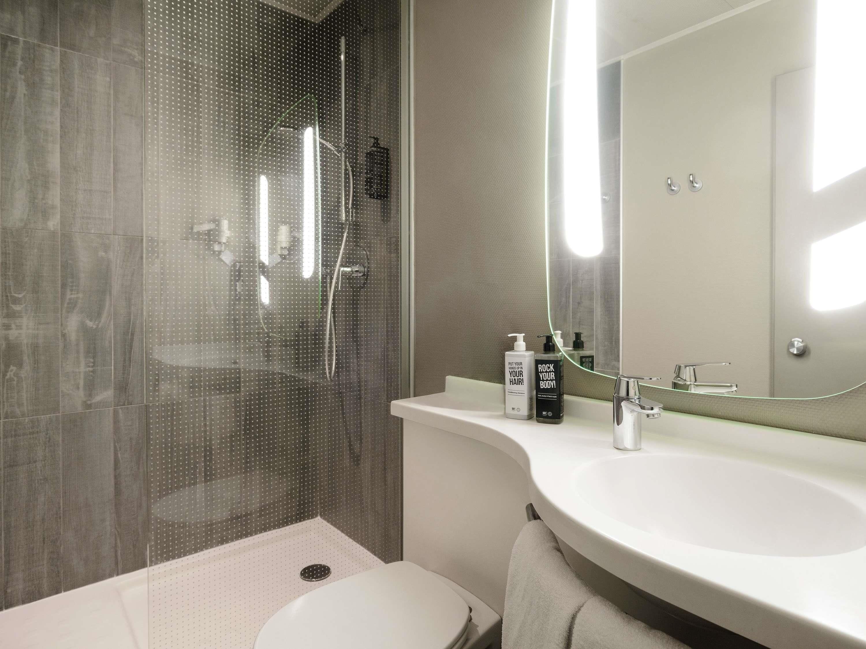 Ein modernes Badezimmer mit einer gläsernen Dusche, einem weißen Waschbecken und einem großen Spiegel.