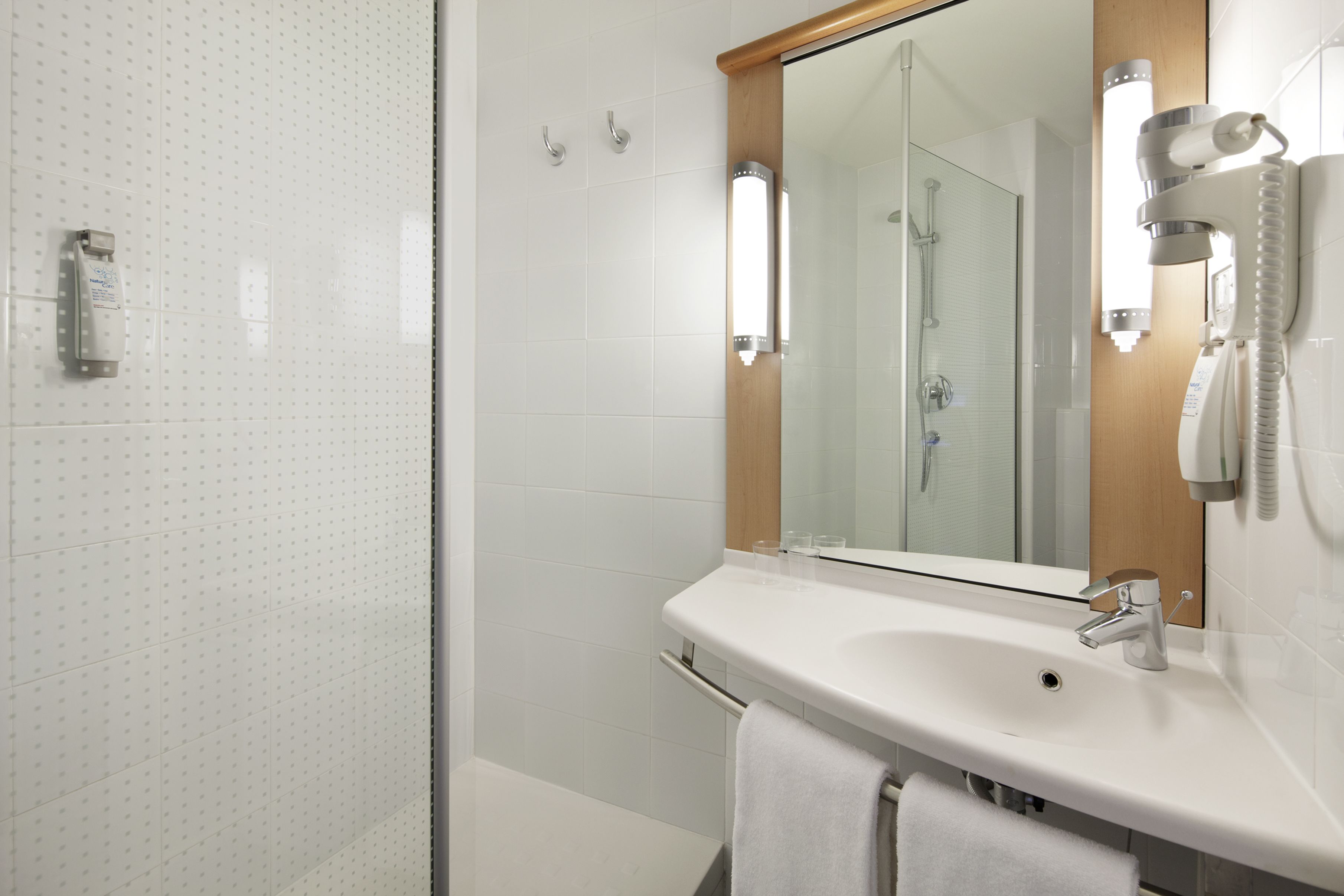Une salle de bain moderne avec un lavabo blanc, un miroir, un porte-serviettes et un espace douche.