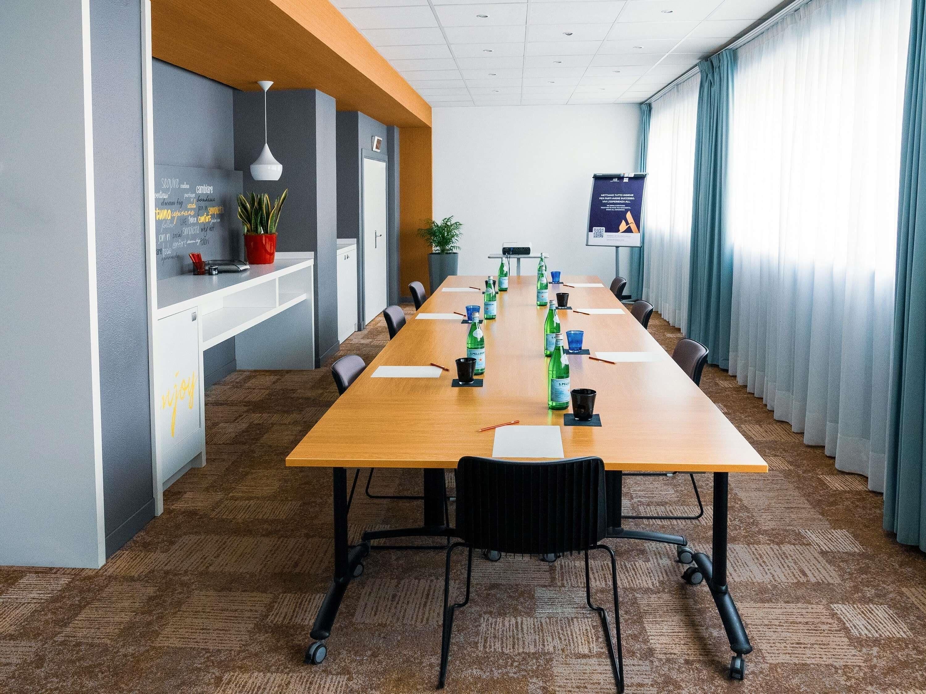 A conference room with a long table, chairs, a potted plant, and a poster on the wall.