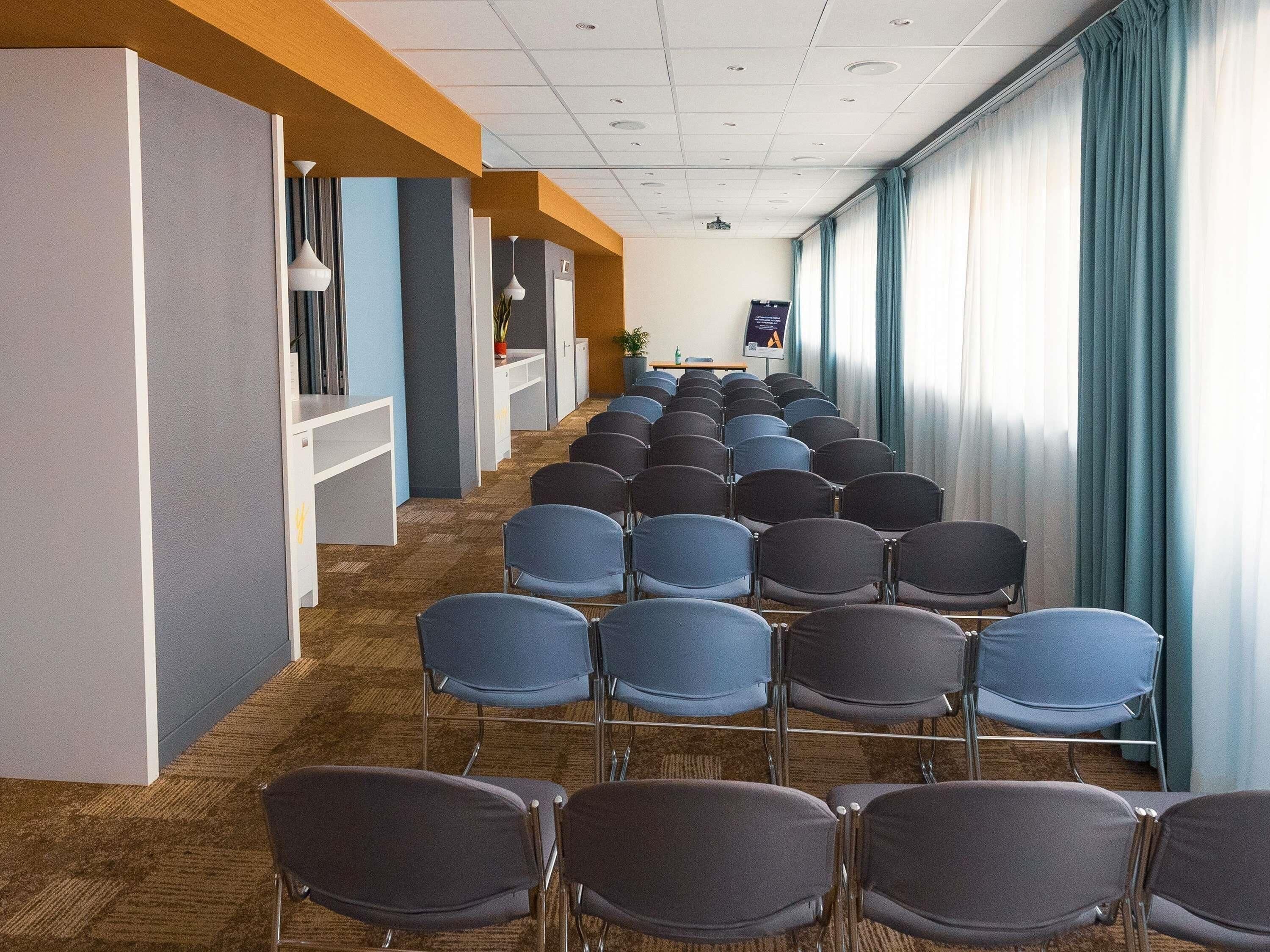 A conference room with rows of chairs, a whiteboard, and a projector screen.