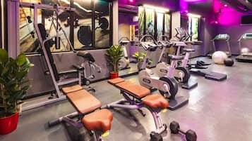 Un gimnasio con equipo de ejercicio, bancos, mancuernas, cintas de correr y un espejo.
