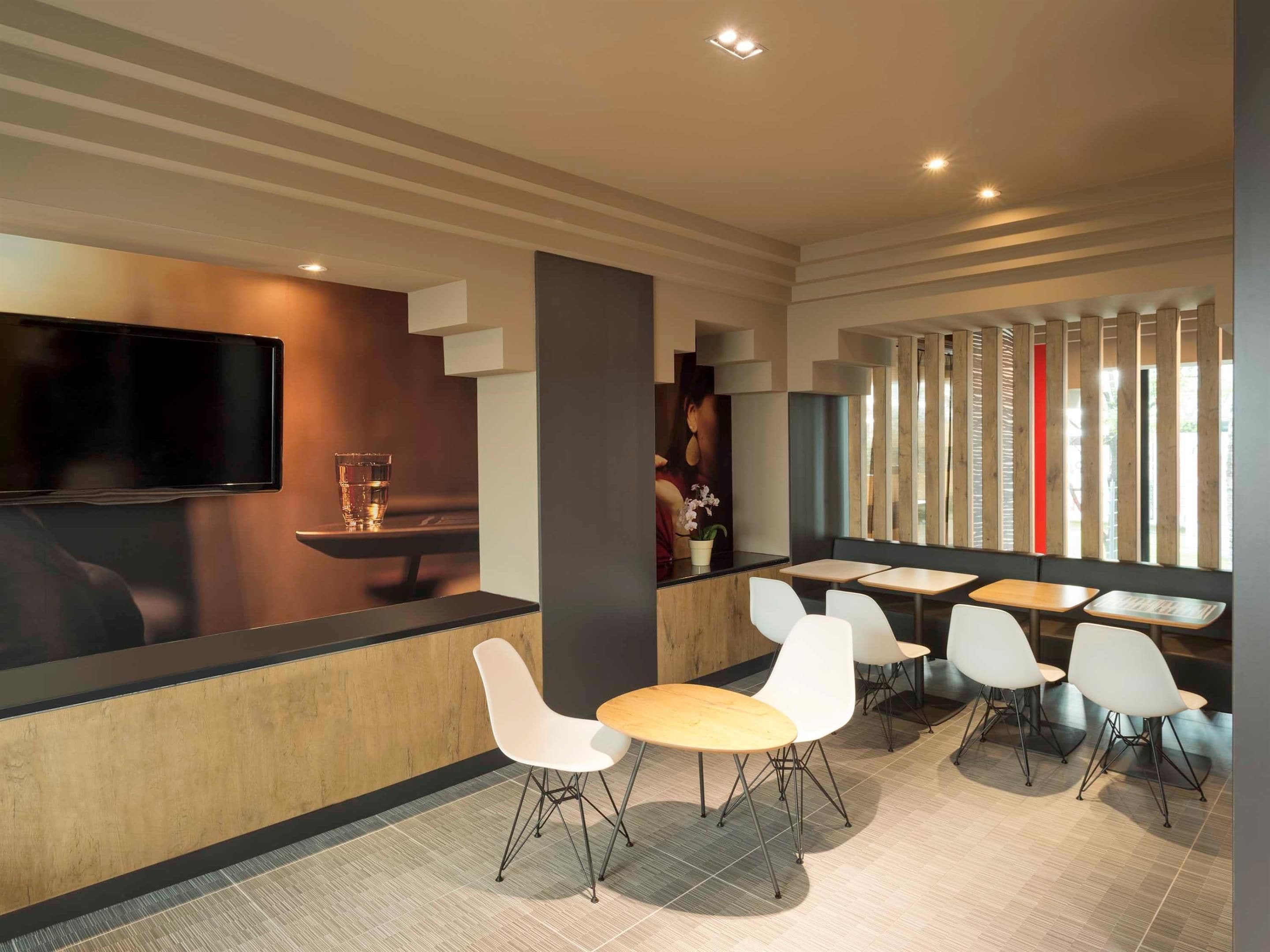 A modern restaurant with a long counter, white chairs, and a TV mounted on the wall.