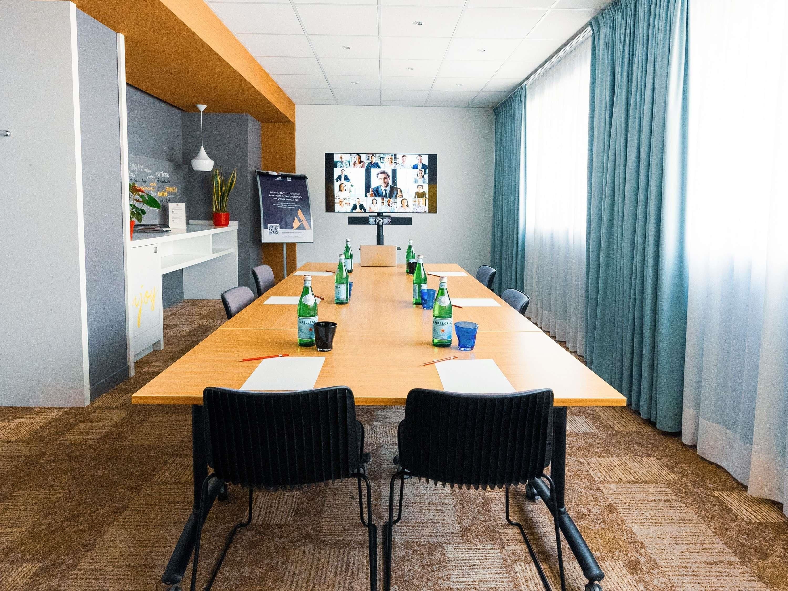 A conference room with a long table, chairs, a screen, and a potted plant.
