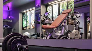 Un gimnasio con equipo de ejercicio, cinta de correr y ventanas amplias con vistas a árboles.