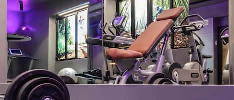 A gym with exercise equipment, a treadmill, and large windows with a view of trees.