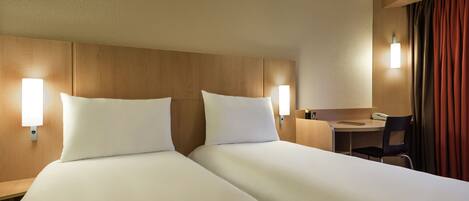 Habitación de hotel con dos camas, un escritorio, una silla y una mesita.