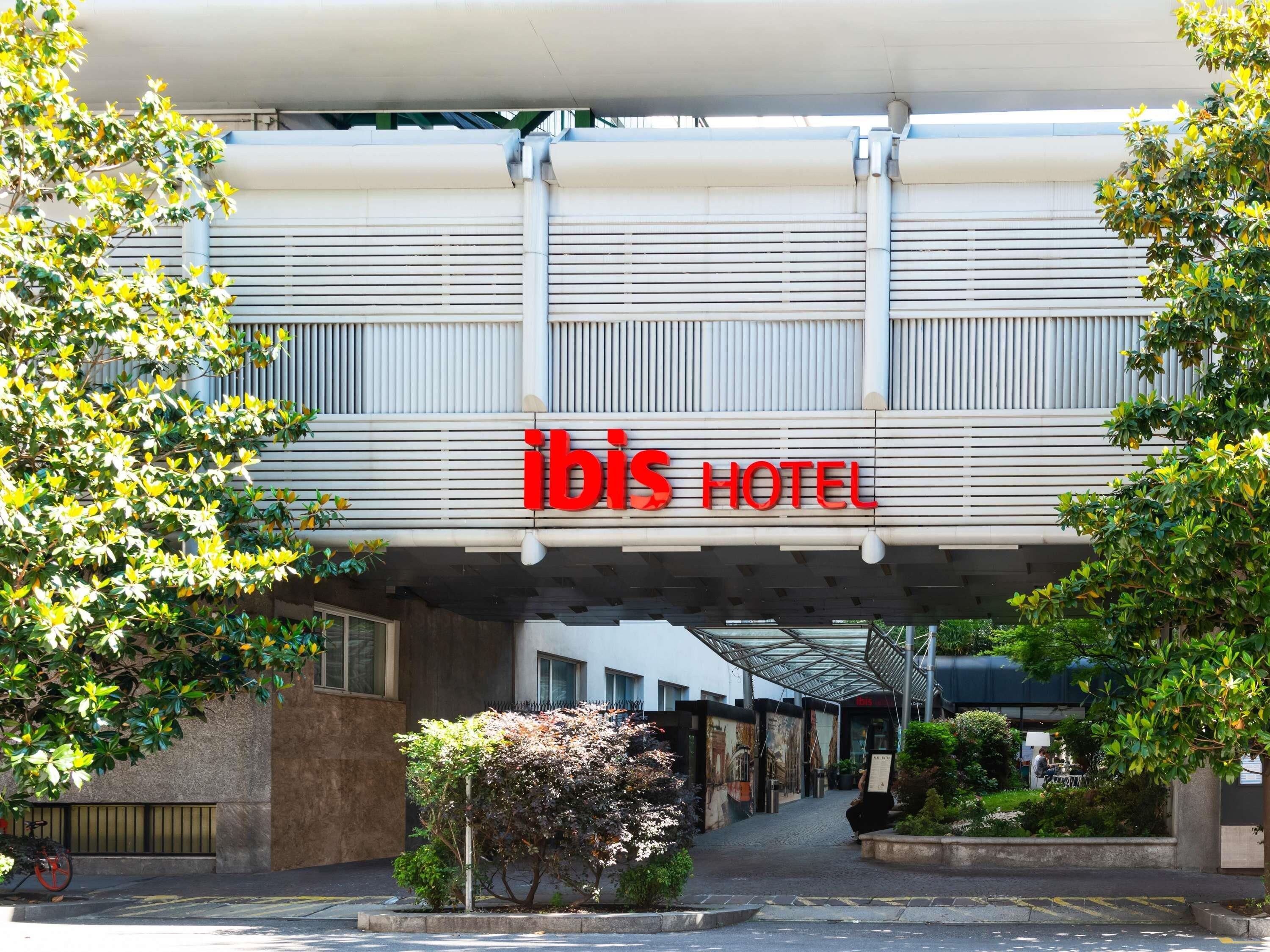 Ein Hotel mit Eingang, einer auffälligen roten Schilder und einem überdachten Zugang, mit Blick auf die Straße.
