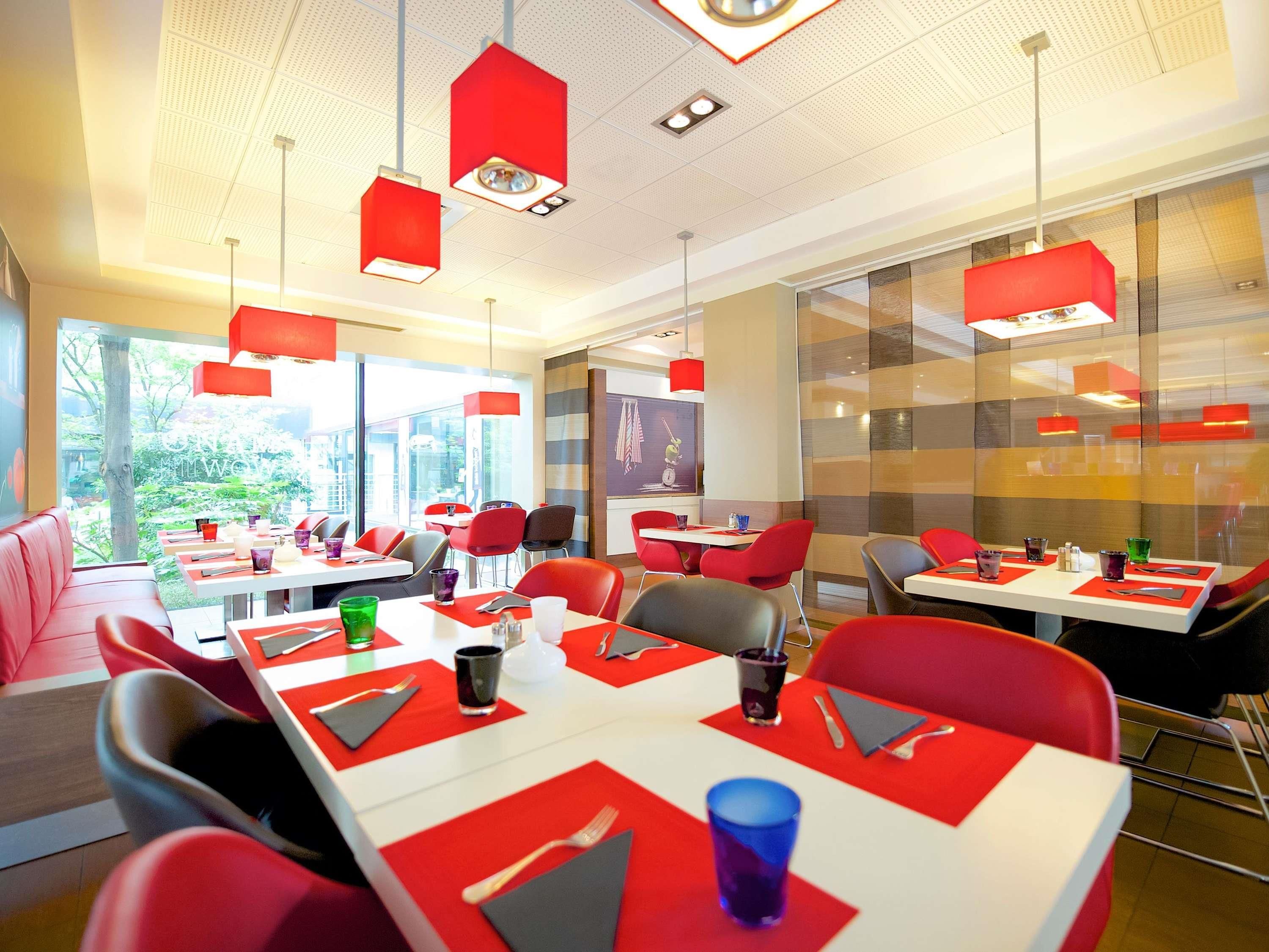 A modern dining area with red chairs and tables, large windows, and red pendant lighting.