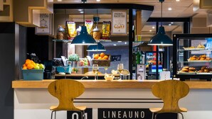 Un bistró con un mostrador que exhibe alimentos, un letrero que dice 'LINEAUNO bistrò & bar' y dos sillas de madera al frente.