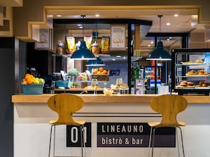 A bistro with a counter displaying food items, a sign for 'LINEAUNO bistrò & bar', and two wooden chairs in front.