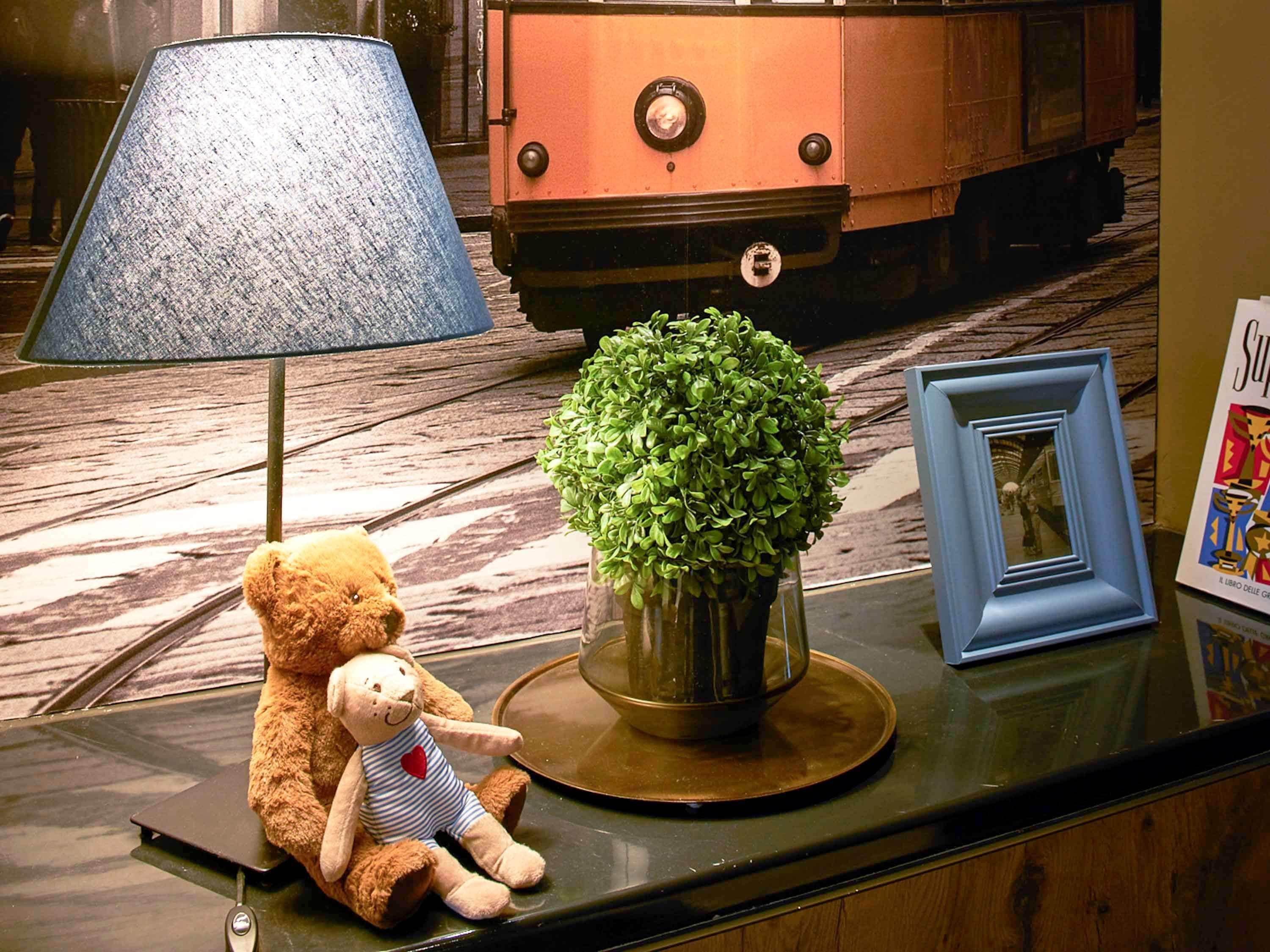 A plush toy, a lamp, a potted plant, and a framed picture on a counter.