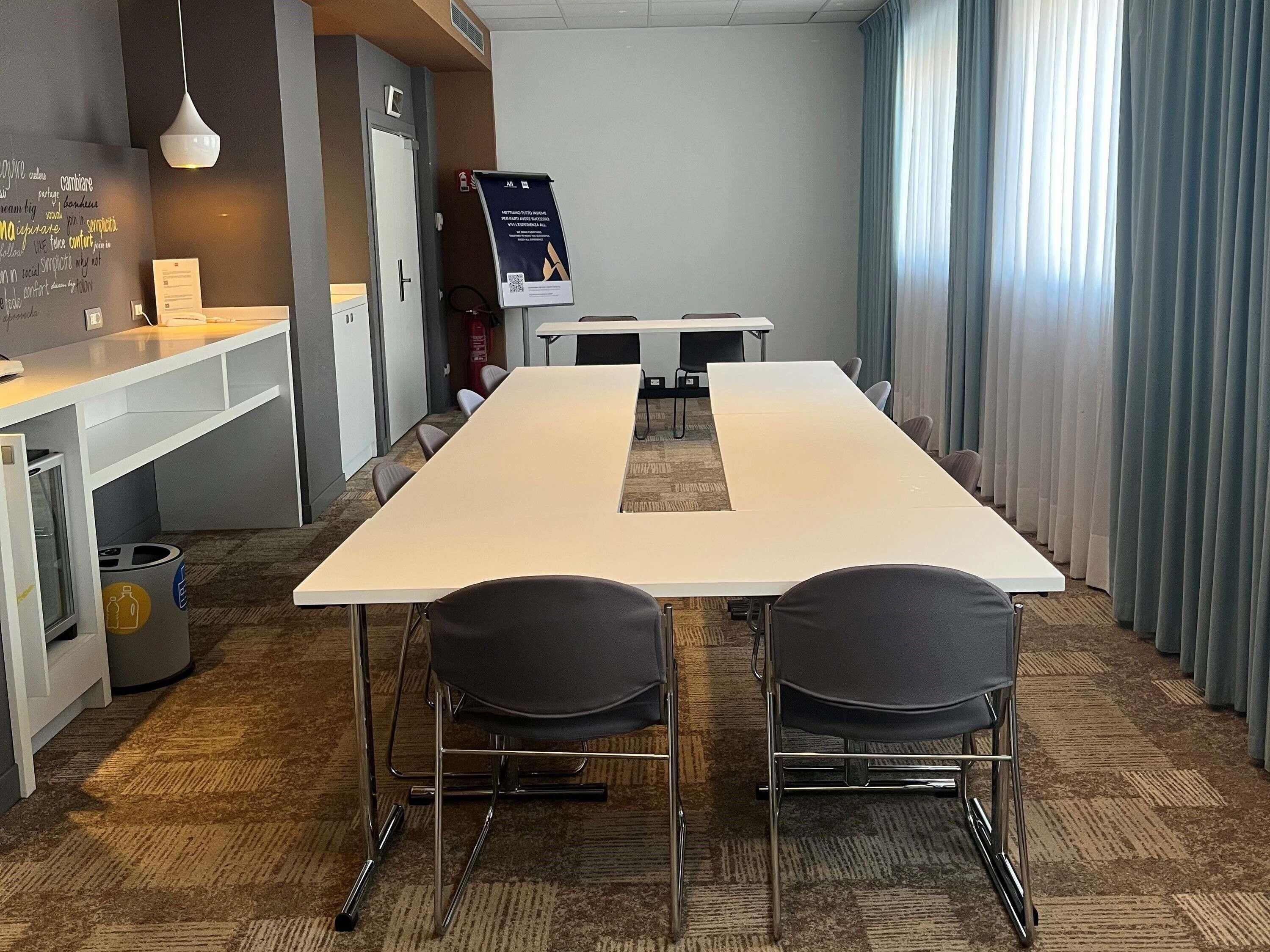 A conference room with a long table, two chairs, a whiteboard, and a digital screen.