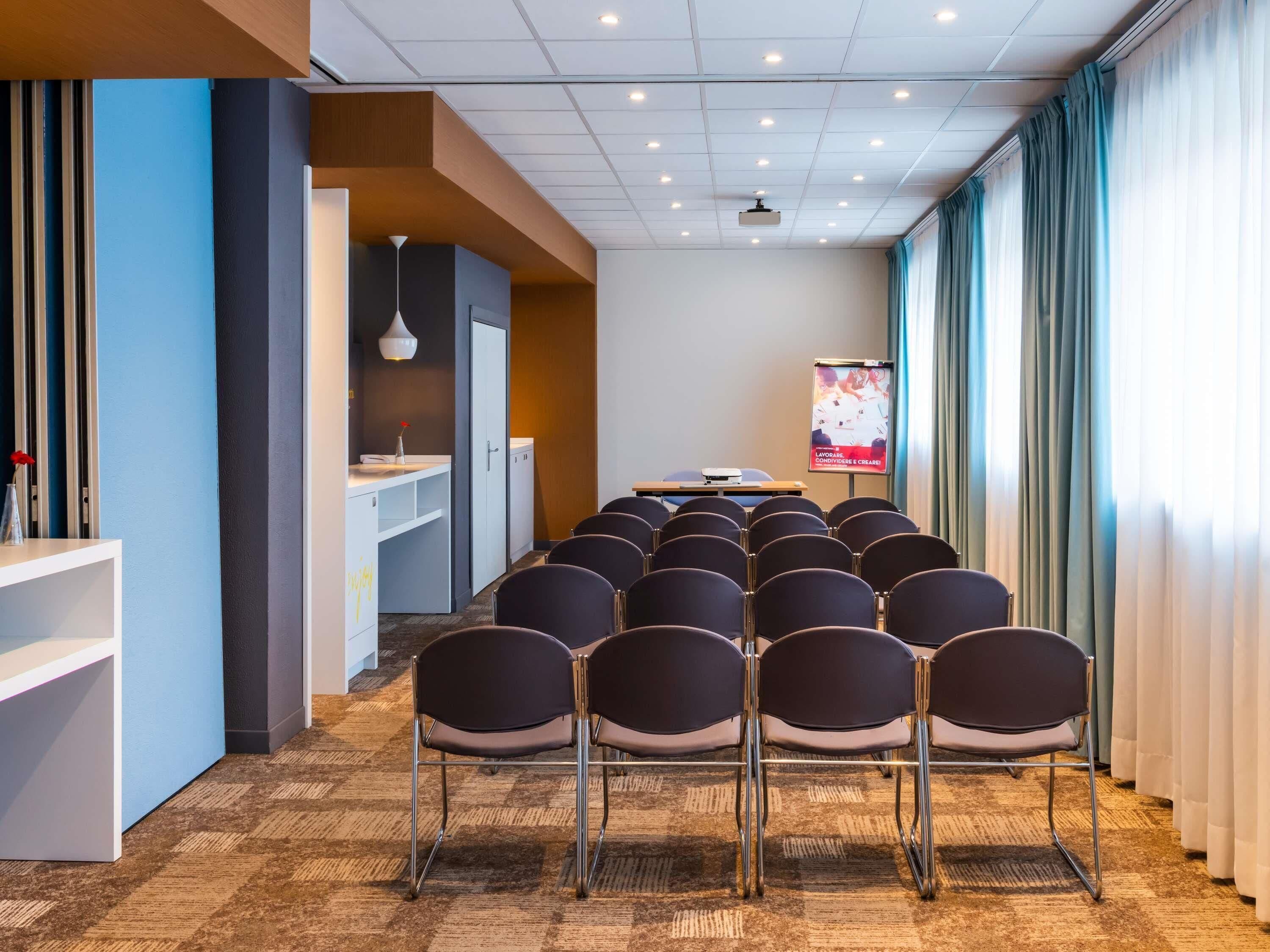 A conference room with rows of chairs, a projector screen, and a whiteboard.