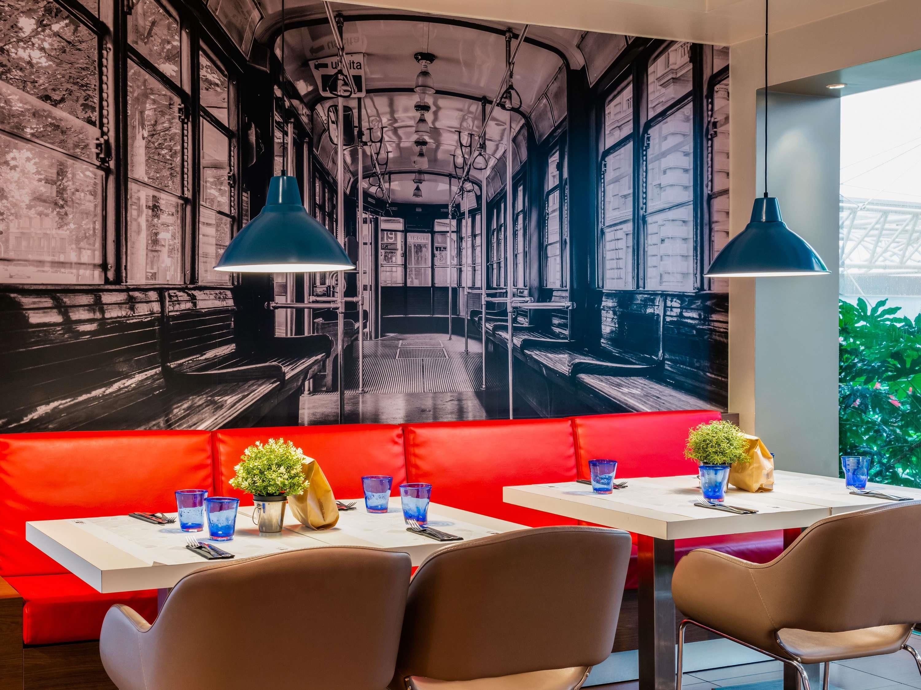 Un ristorante con un murale raffigurante l'interno di un treno, sedute rosse e tavoli con bicchieri e fiori blu.