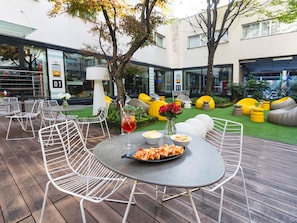 A patio with round tables and white chairs, a pizza plate, and a drink. - ibis Milano Centro (Milan)