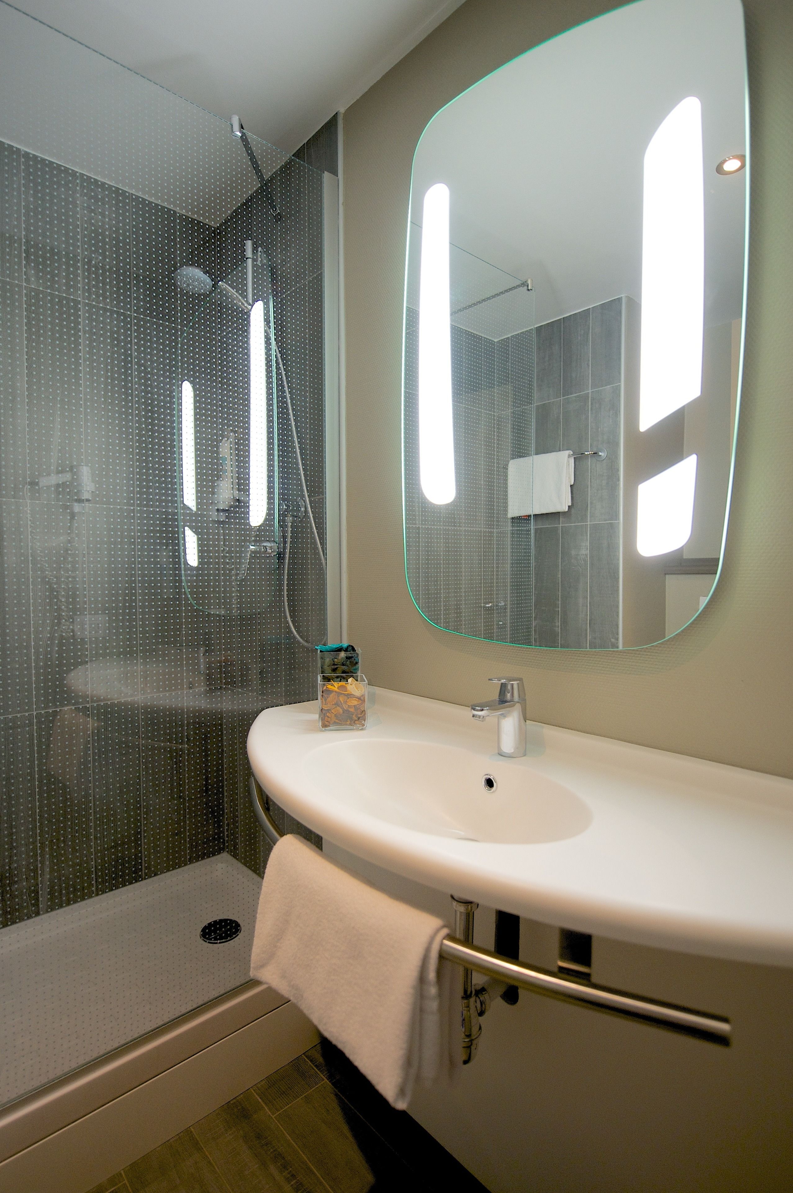 Un bagno moderno con cabina doccia in vetro, un lavandino bianco e uno specchio grande.