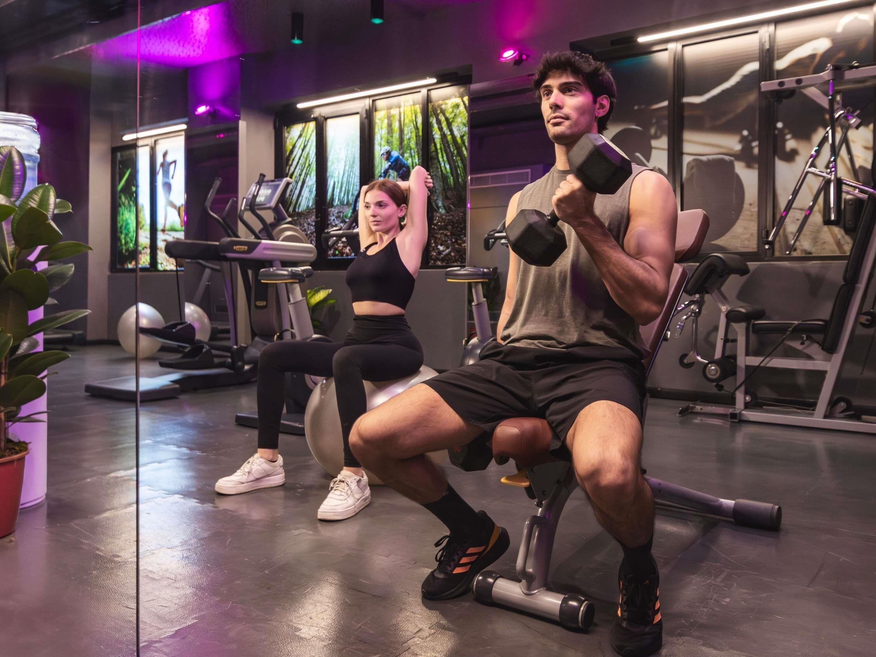 Une salle de sport équipée de matériel d’exercice, d’un tapis de course et où une femme est assise.