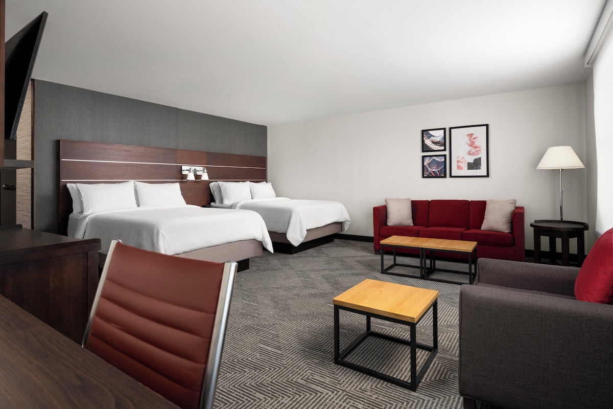 A hotel room with two beds, a red sofa, a wooden coffee table, and a grey armchair.