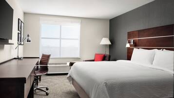 Una habitación de hotel con una cama grande, un escritorio, una silla, un ventanal y un televisor instalado en la pared.