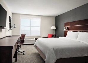 A hotel room with a large bed, a desk, a chair, a window, and a wall-mounted TV.