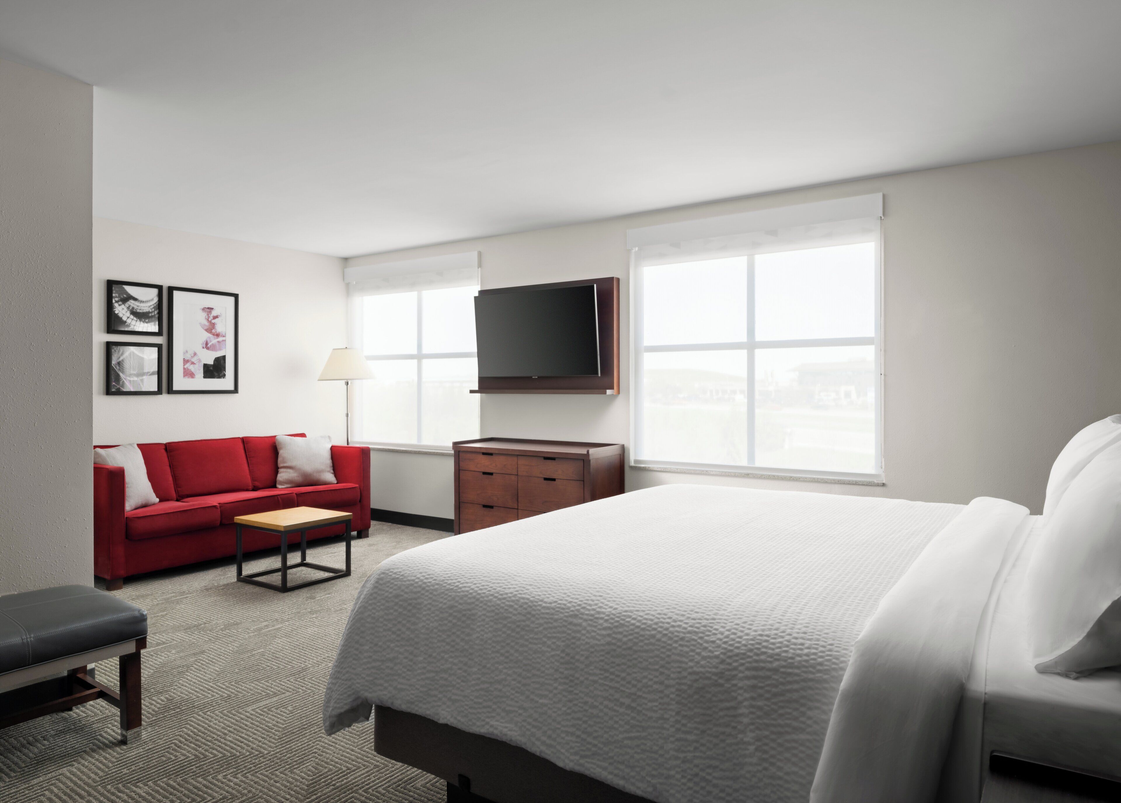 A hotel room with a large bed, a red sofa, a wooden dresser, a flat-screen TV, and framed pictures on the wall.