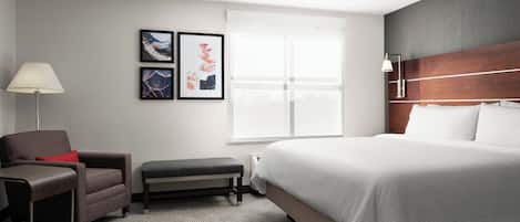 A hotel room with a bed, a desk, a chair, a bench, and a window with blinds.