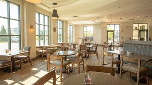 Un restaurant spacieux, doté de nombreuses tables et chaises, de grandes fenêtres laissant entrer la lumière naturelle et d’un intérieur propre et au design moderne.