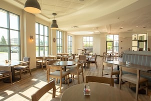 Un restaurante amplio con varias mesas y sillas, ventanas grandes que permiten la entrada de luz natural, y una decoración interior moderna y limpia.