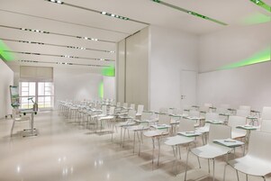 Un'aula moderna con file di banchi e sedie bianche, dettagli verdi sui banchi e un ambiente luminoso e ben illuminato.