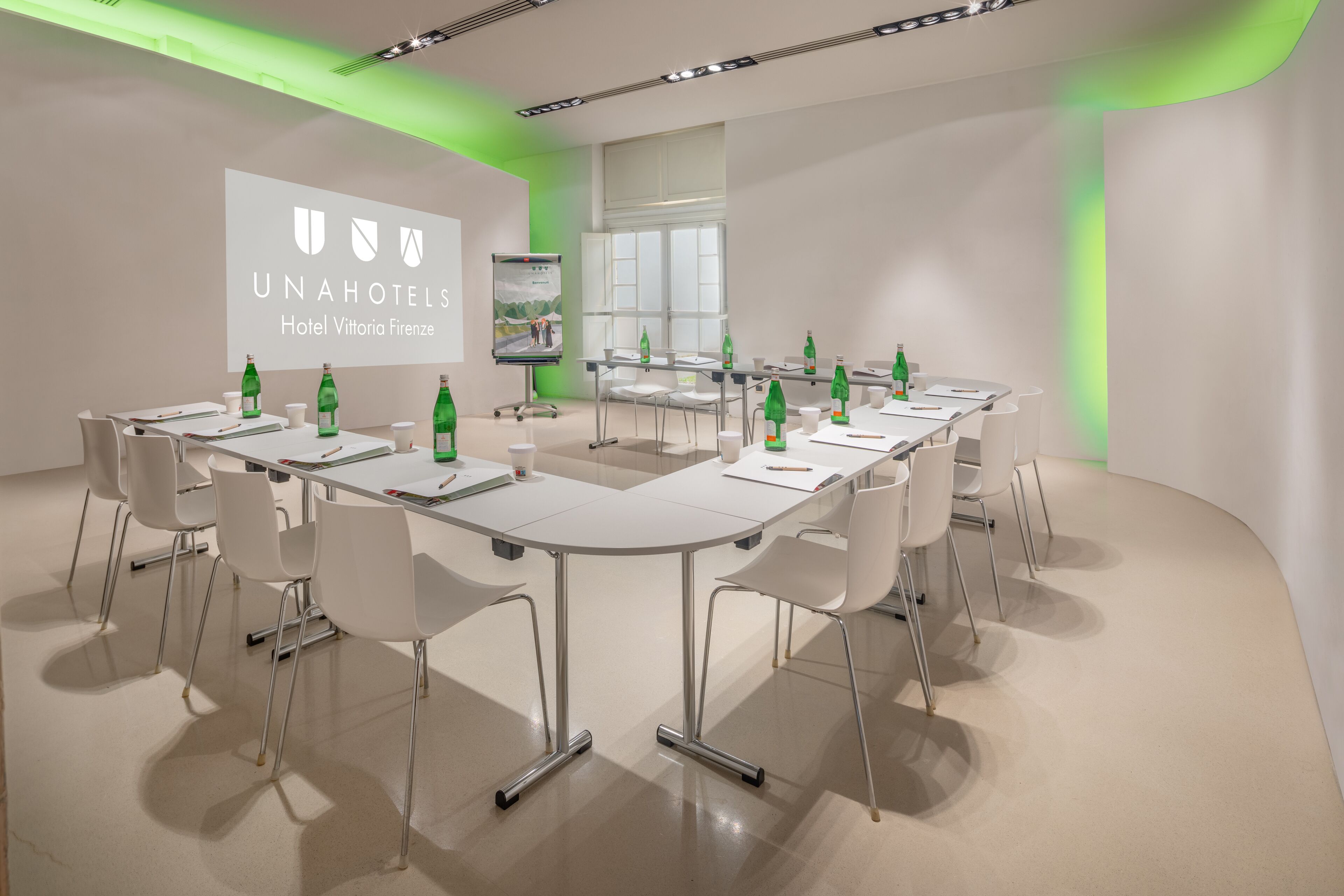 A conference room with a long table, white chairs, and a projector screen displaying the UNAHOTELS logo.