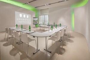 A conference room with a long table, white chairs, and a projector screen displaying the UNAHOTELS logo.