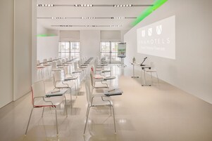 Una sala conferenze con file di sedie bianche, uno schermo di proiezione e un leggio.