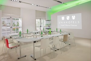 A conference room with white tables, chairs, and a projection screen displaying the logo of UNAHOTELS Hotel Vittoria Firenze.