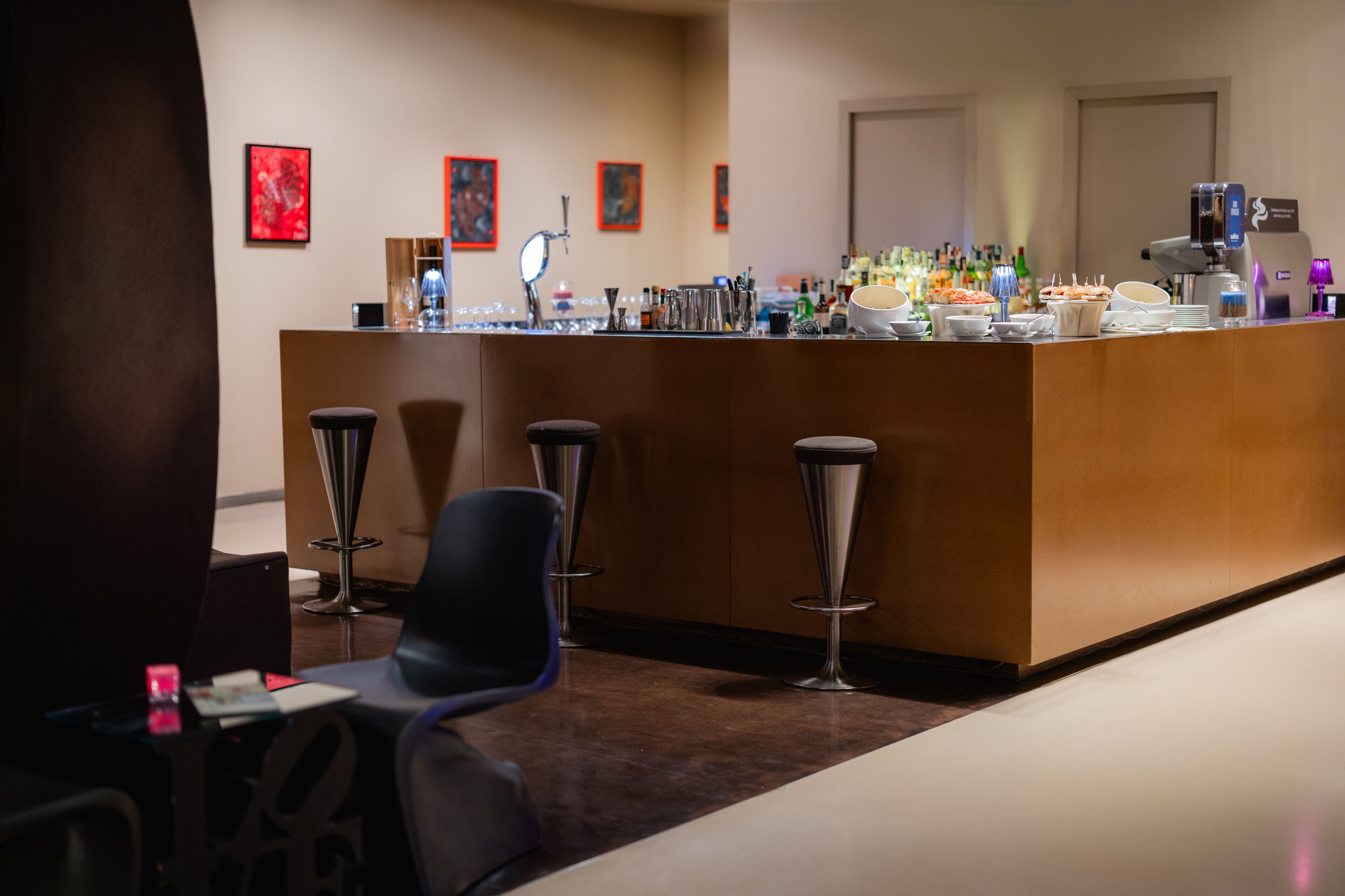 Un espace bar avec des tabourets, un comptoir où sont exposés divers articles, et des œuvres d’art encadrées accrochées au mur.