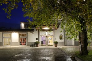 Un edificio con un ingresso lastricato, due piante in vaso e una bicicletta parcheggiata davanti.