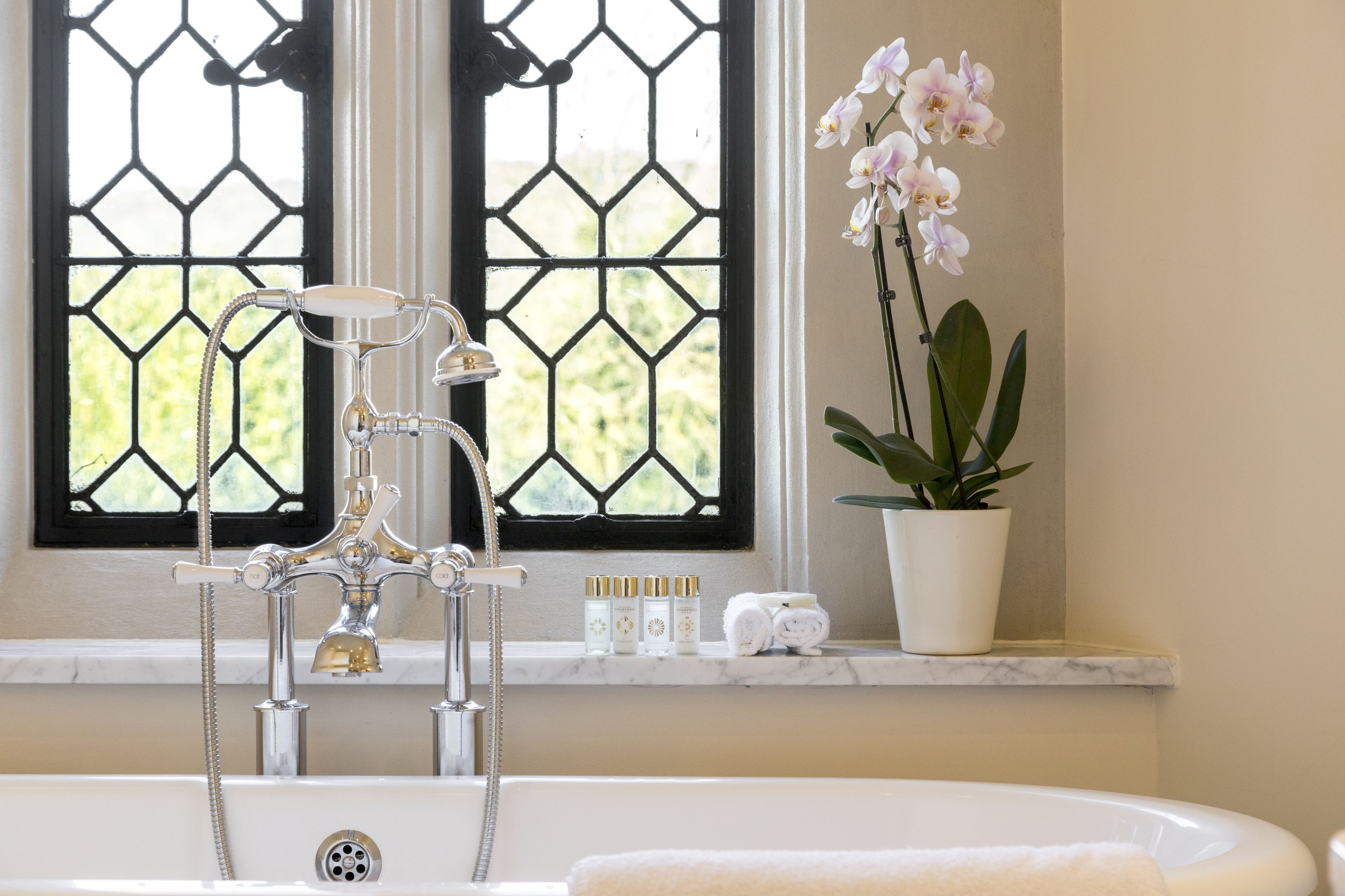 A bathroom with a bathtub, a window with a geometric pattern, a potted orchid, and toiletries on the windowsill.
