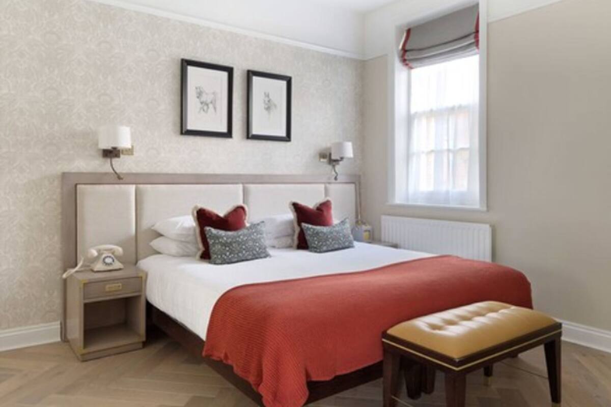 A neatly arranged bedroom with a large bed, bedside tables, a nightstand, a bench, and a window with curtains.