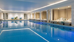 Ein Innenpool mit klarem, blauem Wasser, umgeben von Liegebereichen mit Sitzgelegenheiten und Vorhängen.