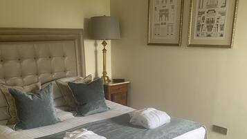 A neatly made bed with pillows, a bedside lamp, and a bench. There are two framed pictures on the wall.