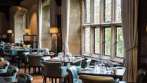 Ein Restaurant mit gedeckten Tischen, großen Fenstern mit schmiedeeisernen Verzierungen und hohen Säulen.