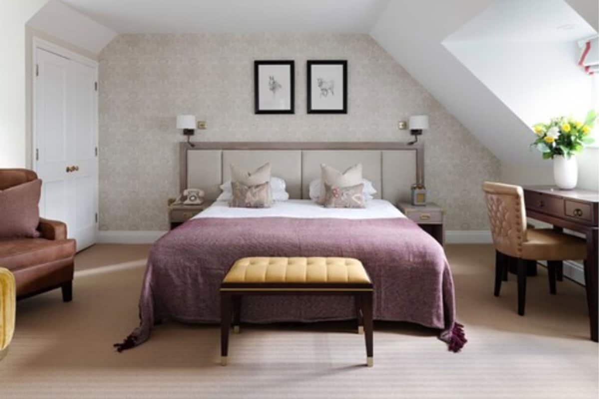 A bedroom with a bed, a bench, a chair, a desk, and a nightstand.