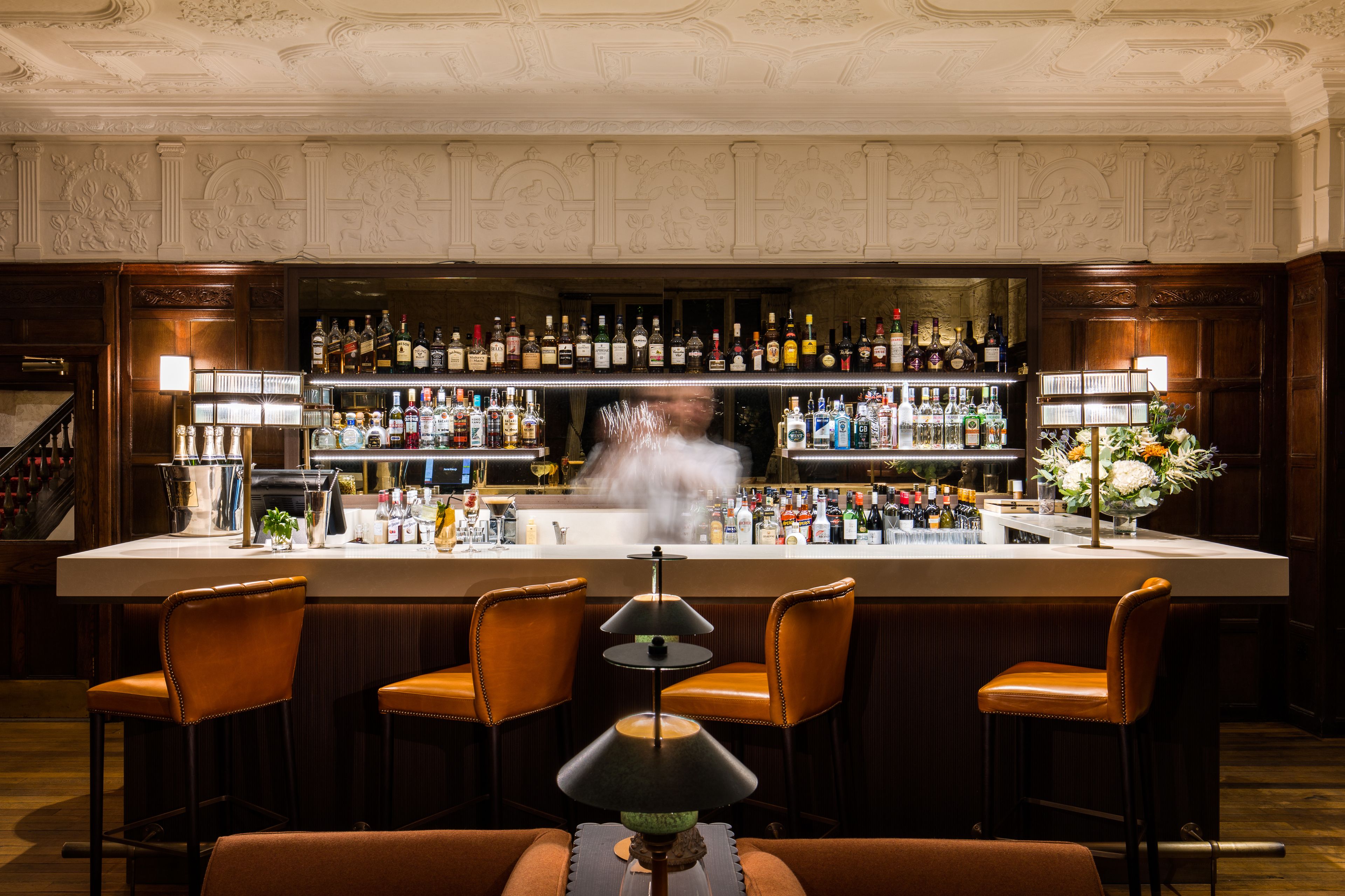 A bar area with a bar counter, multiple liquor bottles, and bar stools.