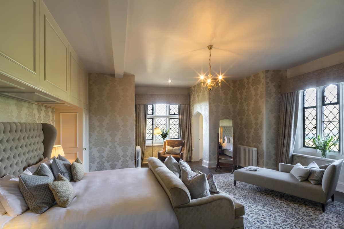 A bedroom with a large bed, a sofa, a chair, and a chandelier.