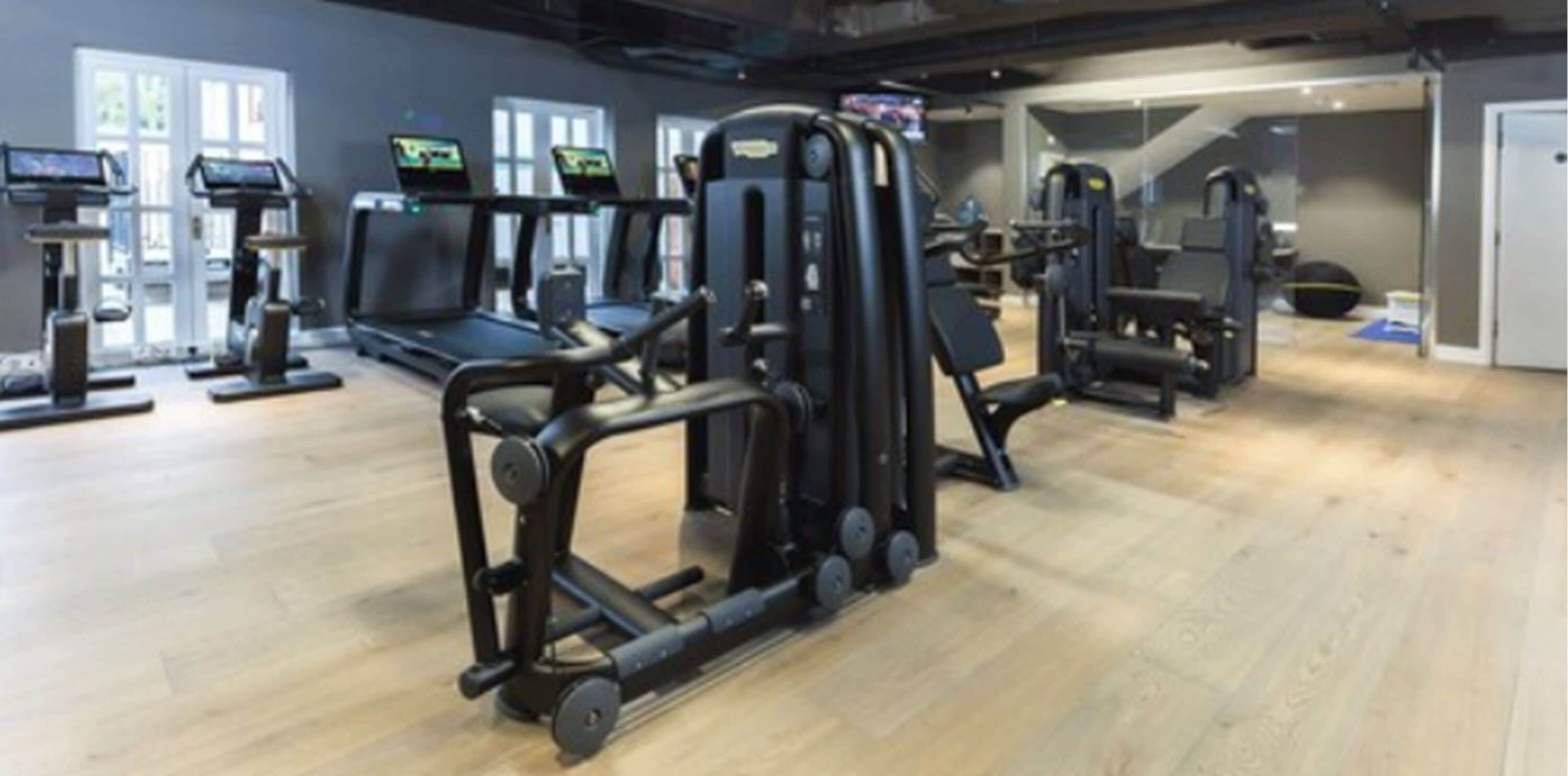 Un gimnasio con cintas de correr, máquinas de pesas y un espejo grande.