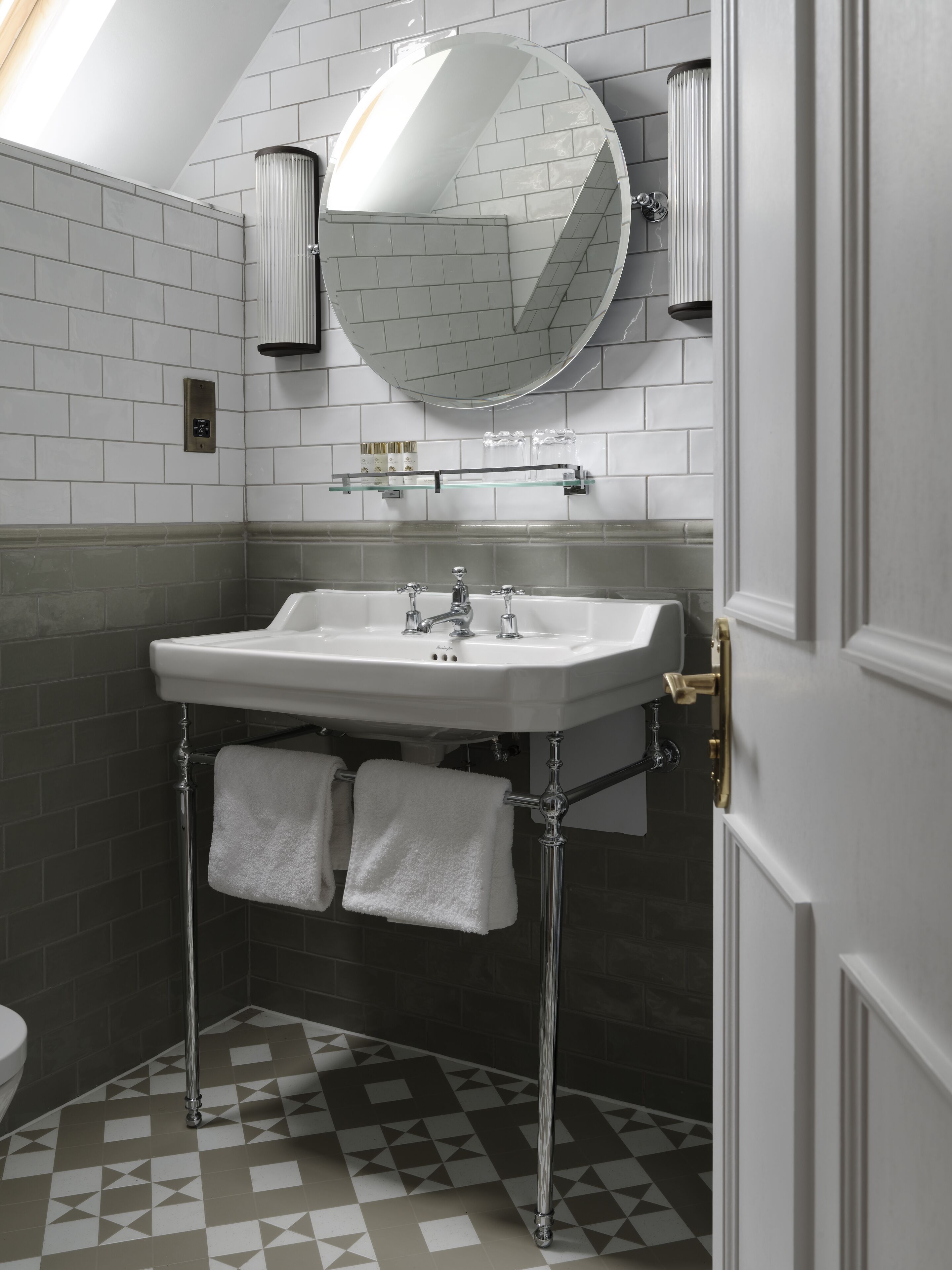 A bathroom with a white sink, two towels, a round mirror, and a tiled floor.