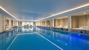 Ein großer, überdachter Pool mit Fliesenboden und -wänden, umgeben von Sitzbereichen mit Kissen und Pflanzen.