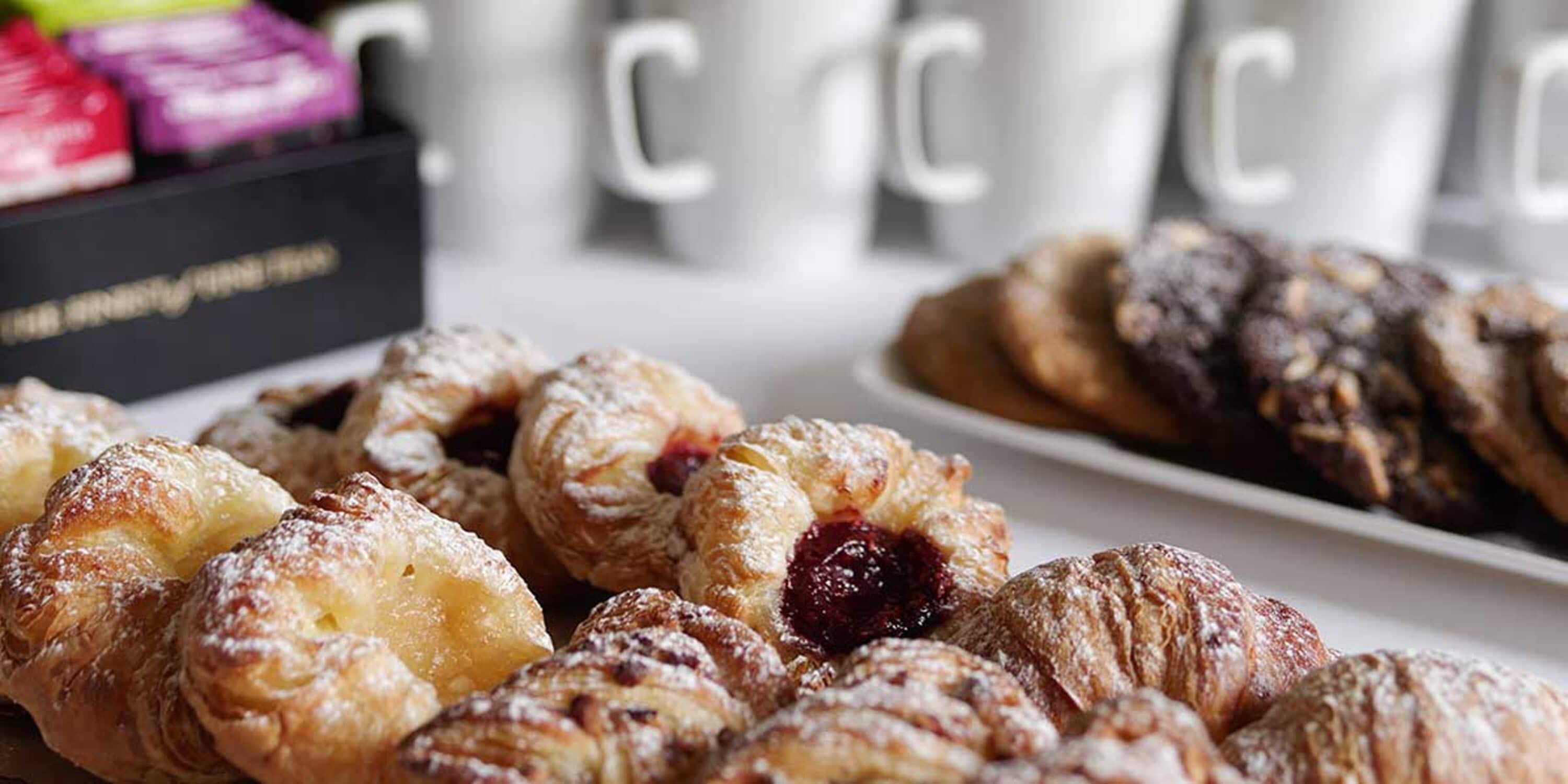 Variedad de pasteles en una bandeja, incluyendo croissants y pasteles con relleno de fruta, exhibidos sobre una mesa.
