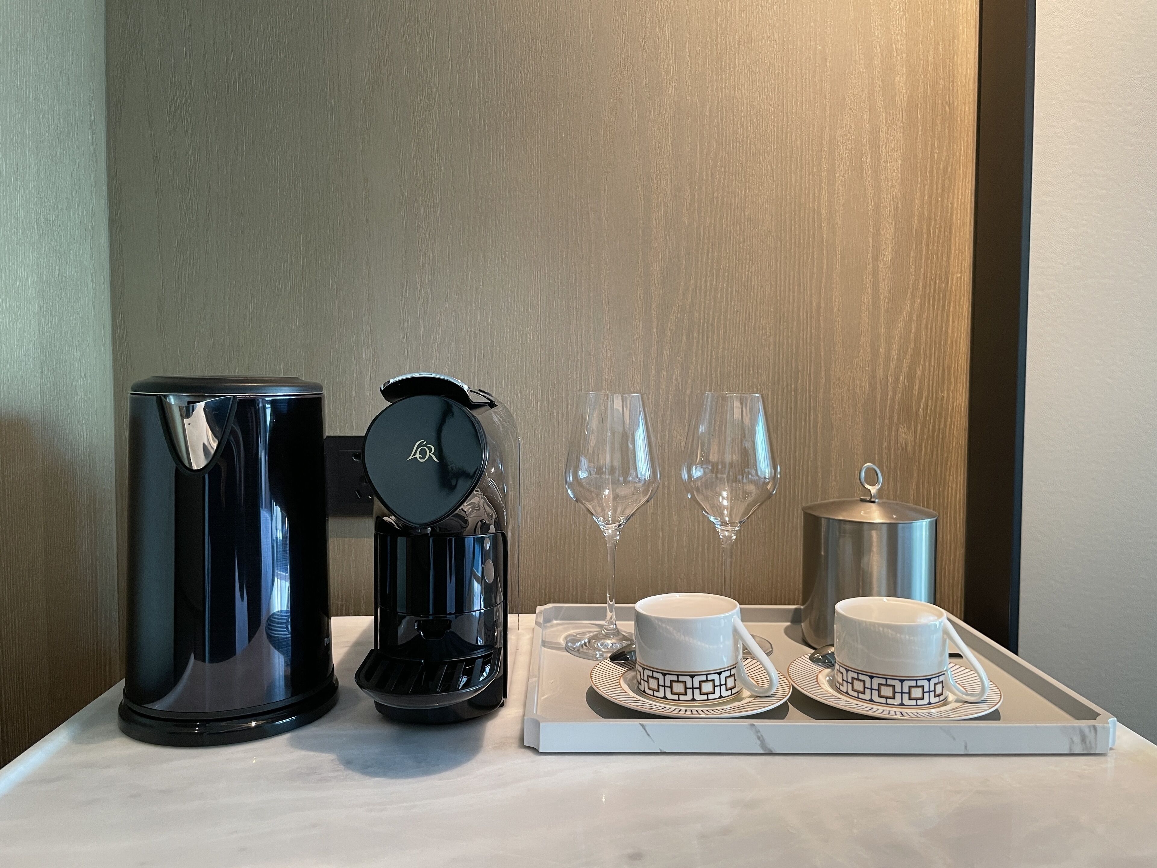 A tray with a coffee maker, two cups, two wine glasses, and a teapot on a marble surface.