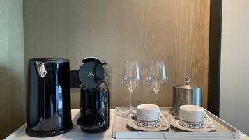A tray with a coffee maker, two cups, two wine glasses, and a teapot on a marble surface.