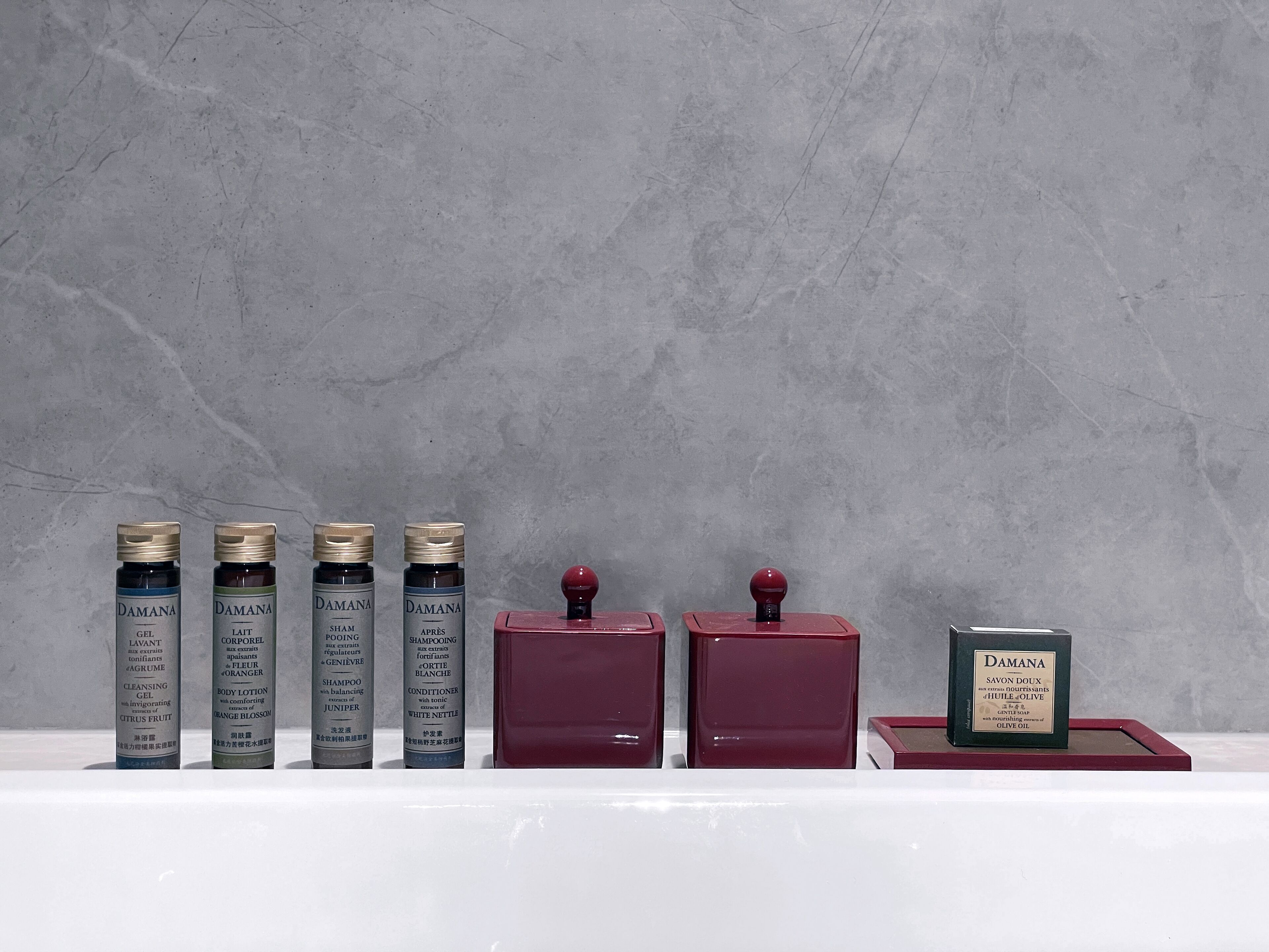 A row of cosmetic bottles and containers on a shelf against a grey wall.